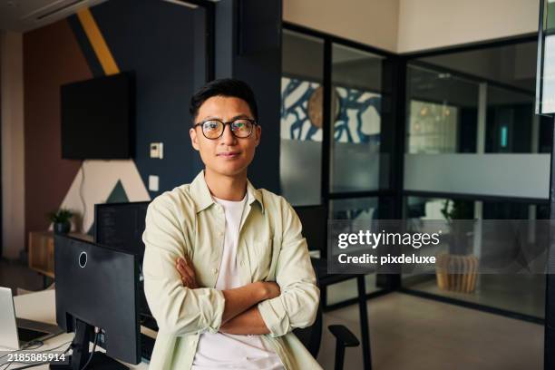 young asian computer programmer sitting with crossed arms in modern office - leader stock pictures, royalty-free photos & images