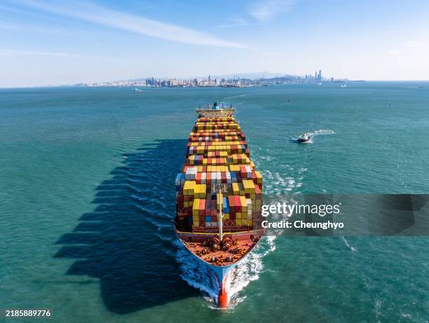 a full cargo ship is sailing in front of qingdao city skyline - schiffbau stock-fotos und bilder