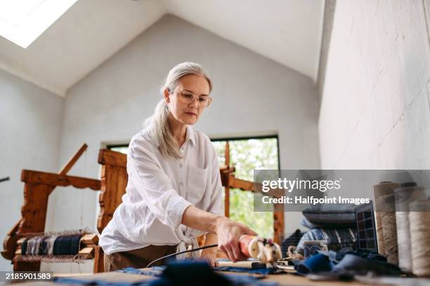 businesswoman working on workbench, preparing fabrics for weaving on wooden loom. upcycling old fabrics and textile in weaving small business. circular economy. - webstuhl stock-fotos und bilder