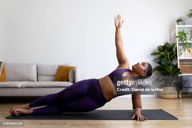 young black woman doing side plank yoga pose at home - entrenamiento-sin-material fotografías e imágenes de stock