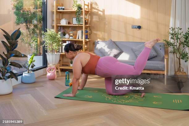 beautiful plus size woman doing stretching on exercise mat in living room at home. - entrenamiento-sin-material fotografías e imágenes de stock