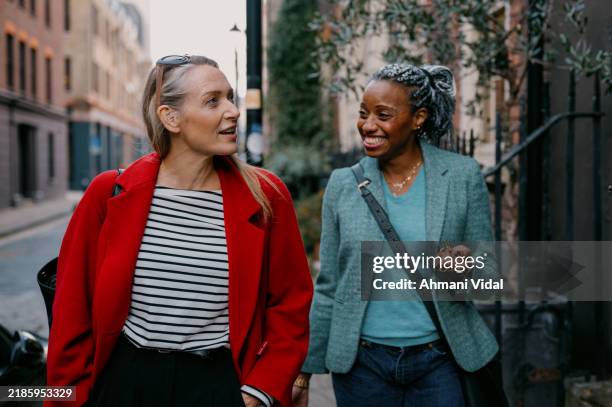 mature friends walk down the street together with their luggage in hand looking for their vacation rental - female friendship stock pictures, royalty-free photos & images