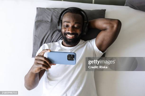 high angle view of african american man lying in bed and consuming online content - serviço de distribuição digital contínua imagens e fotografias de stock