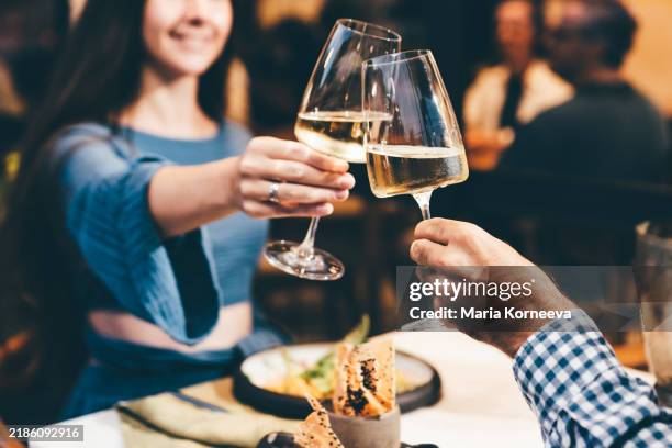 toasting with white wine on a romantic date night. couple drinking white wine and toasting. - table for two stock pictures, royalty-free photos & images