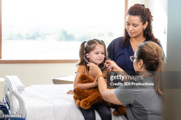 kinderarzt steckt dem jungen patienten spielerisch ein stethoskop in die ohren - notfallmedizin stock-fotos und bilder