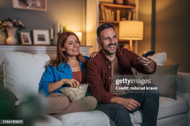 a husband and wife are watching a movie at night and eating popcorn in the living room. - avondschemering stockfoto's en -beelden