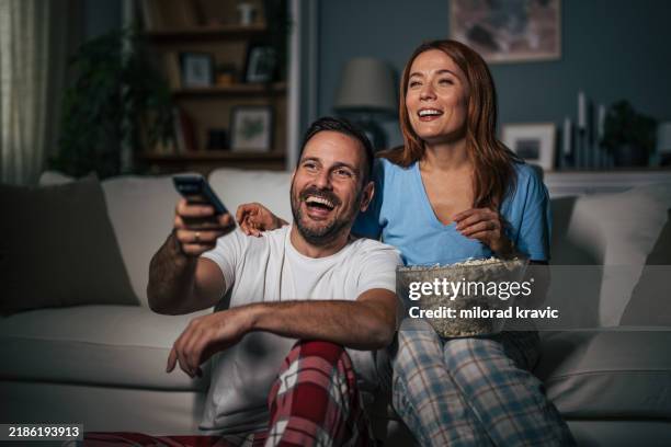 a husband and wife are watching a movie at night and eating popcorn in the living room. - couple pyjamas night stock pictures, royalty-free photos & images