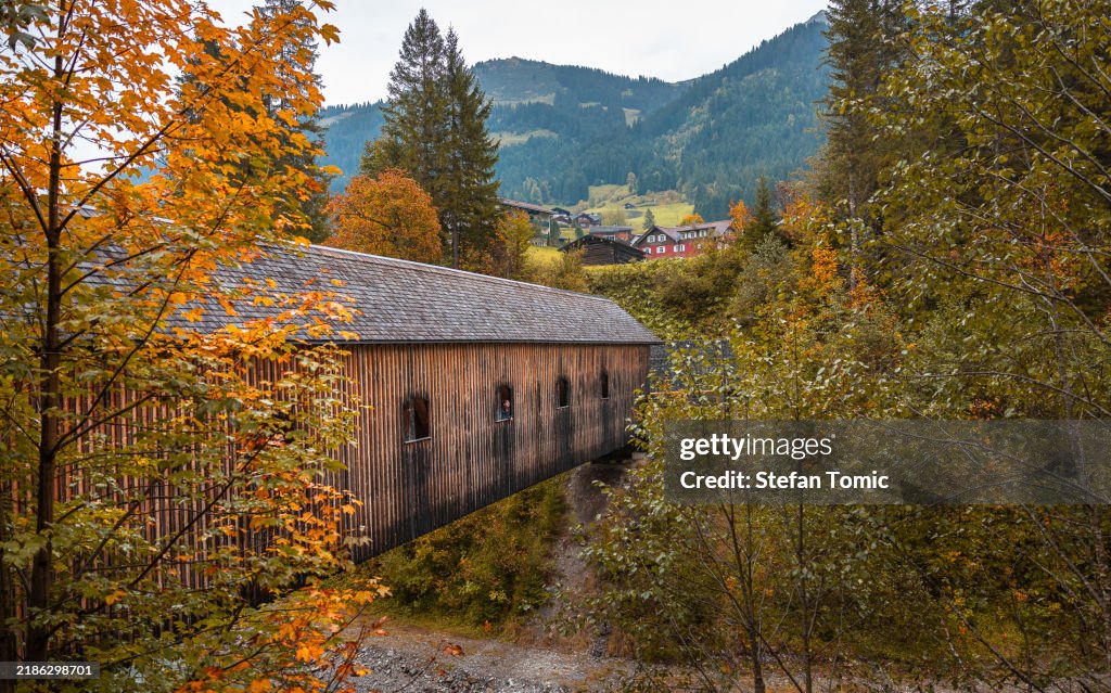 Woman looking out of the window of a covered wooden bridge in the Austrian Alps