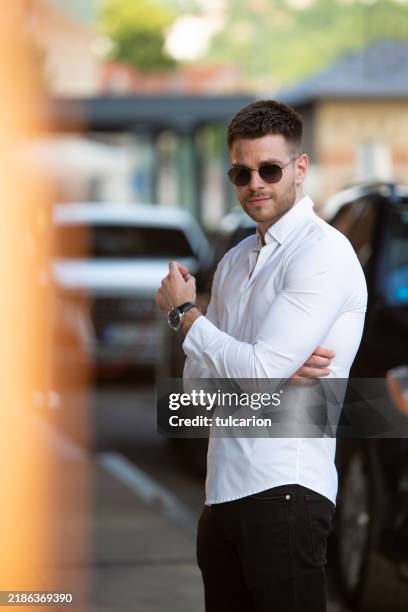 confident young business man standing next to his luxury car in front of a modern hotel - white shirt stock pictures, royalty-free photos & images