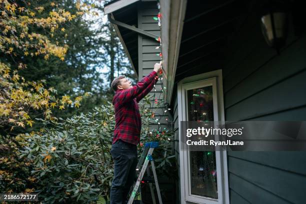 man putting up christmas lights on home exterior - christmas lights stock pictures, royalty-free photos & images