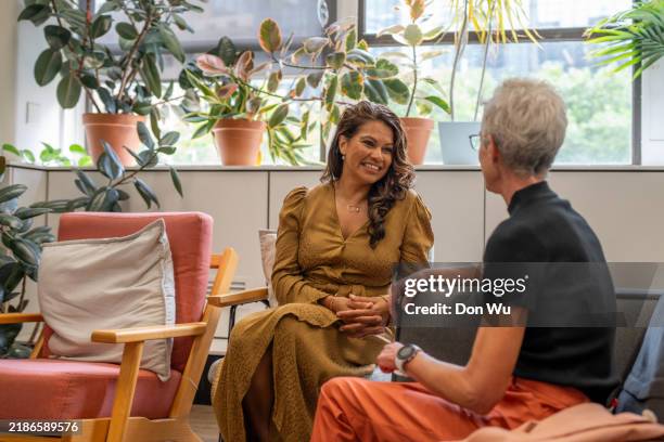 two women having a conversation in a modern lounge - work wellness stock pictures, royalty-free photos & images