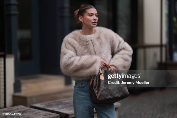 Sophia Geiss is seen wearing two different-sized gold hoop earrings, a silver nose ring, a cropped beige faux fur jacket with wide sleeves from...