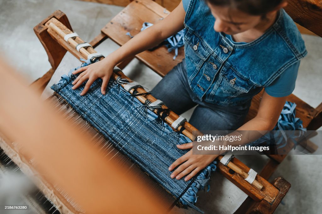 Teenage girl learning how to weave handmade products on traditional wooden loom. Girl helping in family business workshop.