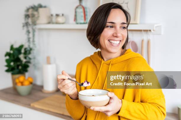 woman enjoying healthy breakfast with yogurt and berries in kitchen - comidas y bebidas fotografías e imágenes de stock