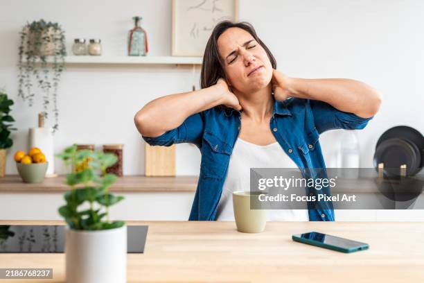 woman suffering from neck pain at home kitchen table - fibromialgia fotografías e imágenes de stock