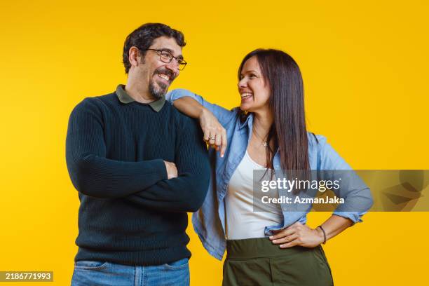 cheerful couple sharing a laugh on yellow background - medium shot stock pictures, royalty-free photos & images