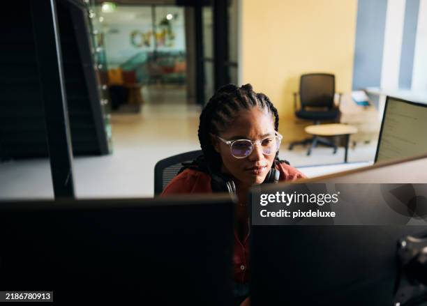 young woman programmer focused on her work, coding on dual monitors in a modern office environment - programmer team stock pictures, royalty-free photos & images
