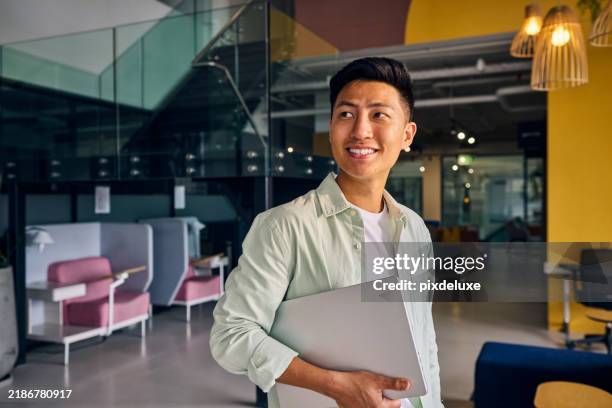 young asian freelancer smiling and holding laptop in modern office - young men stock pictures, royalty-free photos & images