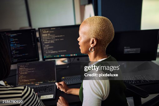 Programmers working together on code using multiple screens and laptop in office Programmers working together on code using multiple screens and laptop in office