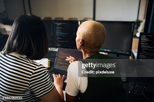 Programmers working together on code using multiple screens and laptop in office Programmers working together on code using multiple screens and laptop in office