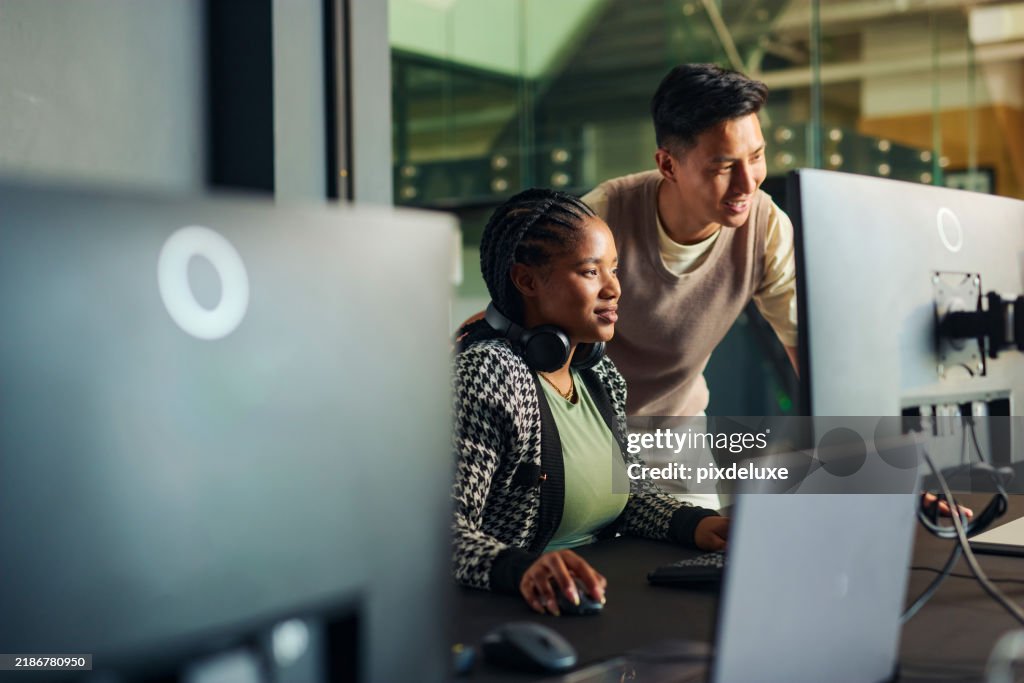 Software engineers collaborating on a project, analyzing code on computer monitors in office
