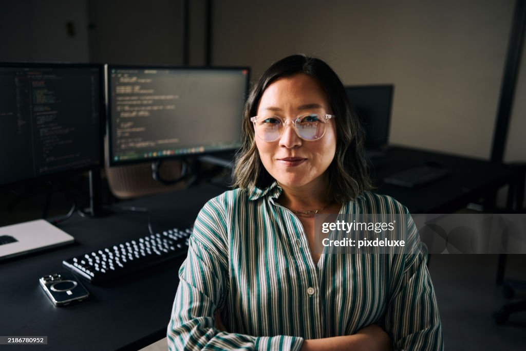 Asian female programmer working on multiple computer screens in modern office