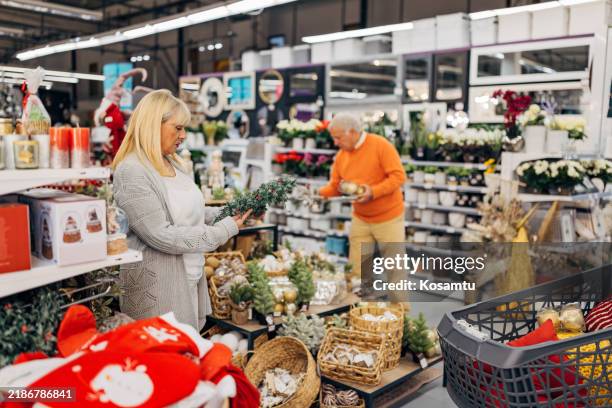 a senior couple dressed in casual clothes enjoys shopping for new year's and christmas decorations in a department store. they look at the displayed christmas ornaments and decorations - new look store stock pictures, royalty-free photos & images