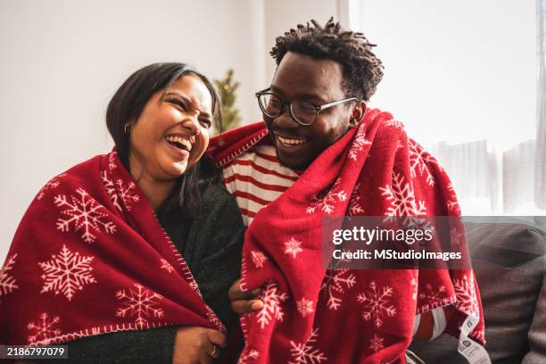 joyful couple laughing while wrapped in festive red blanket - festieve stemming stockfoto's en -beelden