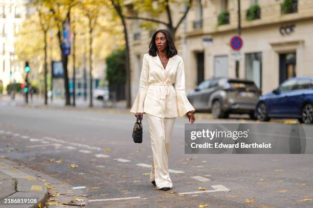 Dafa Traore wears a white satin lustrous silky jacket and pants / suit from Shona Joy, a Lady Dior black leather quilted bag, Dior pointed shoes,...