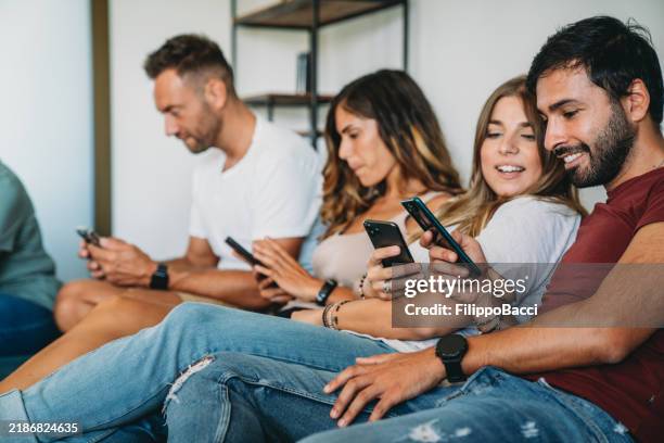 eine gruppe von freunden benutzt smartphones zu hause auf dem sofa - sportwetten stock-fotos und bilder