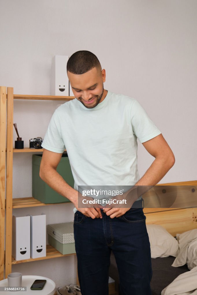 Young man buttoning his jeans in bedroom