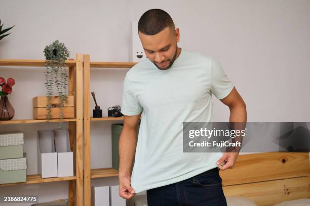 junger mann probiert zu hause hellgrünes t-shirt an - anziehen stock-fotos und bilder