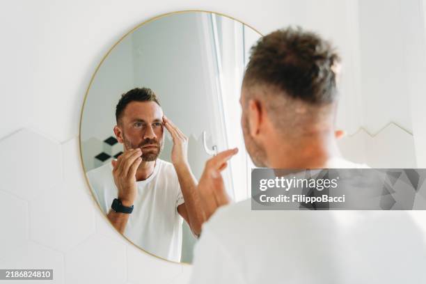 un hombre millennial está usando una crema facial en el baño - vanidad fotografías e imágenes de stock