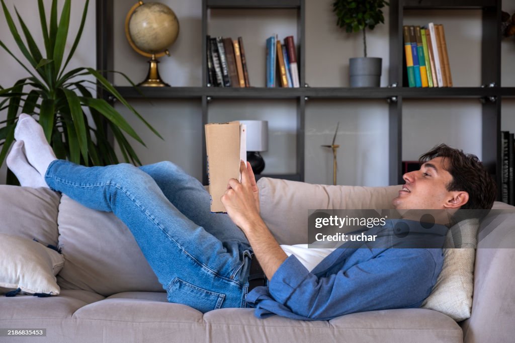 Young man relaxing on sofa reading a book at home