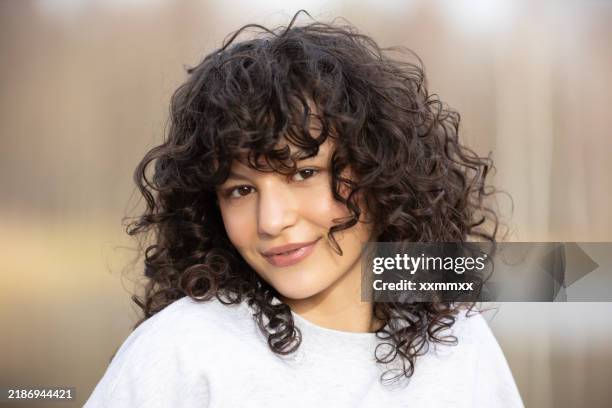 a beautiful girl with dark curly hair is relaxing outdoors and smiling - curly hair stock pictures, royalty-free photos & images