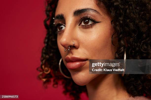 non-binary person contemplating against red background - pendiente de la nariz fotografías e imágenes de stock