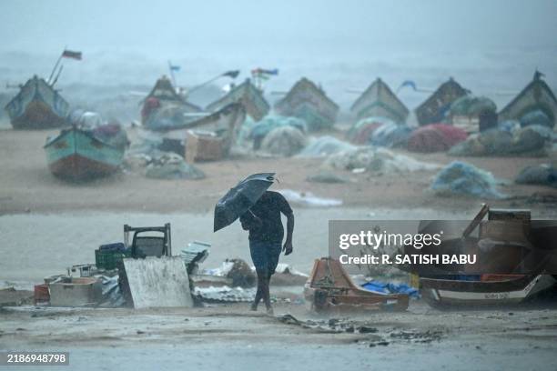 Man holding an umbrella walks amidst heavy winds and rainfall at Marina Beach in Chennai on November 30 ahead of the landfall of cyclone Fengal in...