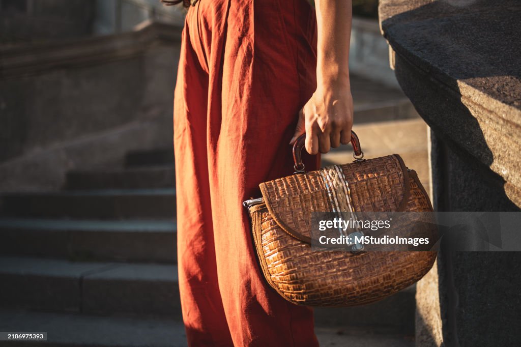 Donna alla moda in abito rosso che tiene una borsa tessuta alla moda