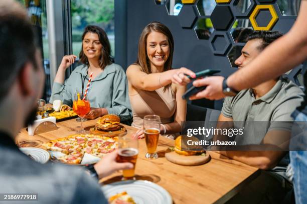 young woman paying via contactless channel by mobile banking application - pub food stock pictures, royalty-free photos & images