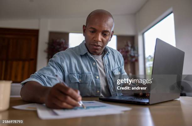 man working at home on his laptop and writing on documents - plano de atividades imagens e fotografias de stock