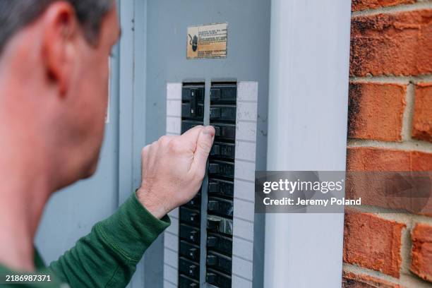 vue par-dessus l’épaule d’un homme vérifiant un disjoncteur sur un panneau extérieur de boîte à fusibles électrique - tableau de commande photos et images de collection