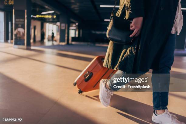 traveler walking with suitcase in sunlit airport terminal - wheeled luggage stock pictures, royalty-free photos & images