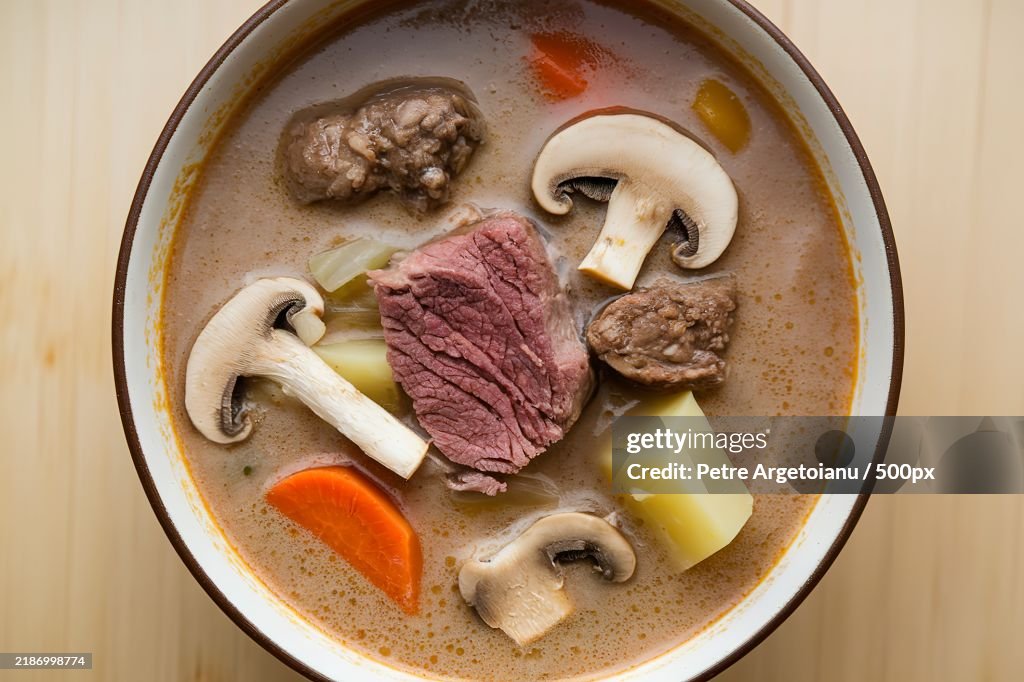 A bowl containing creamy soup with mushrooms,Chunks of beef,And vegetables