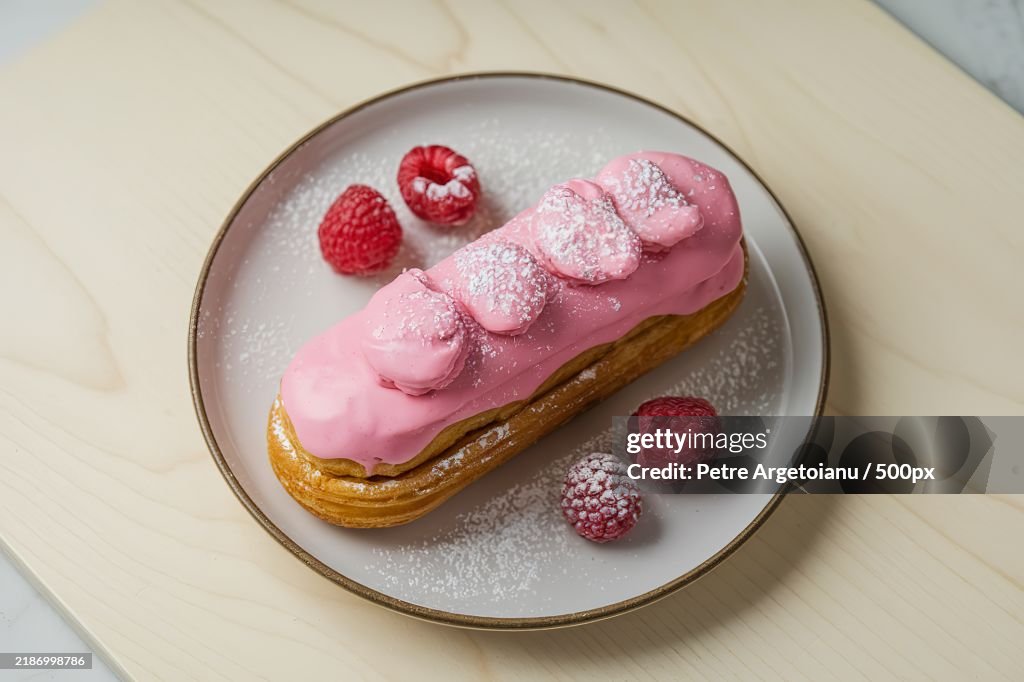 A photo of an eclair dessert with pink icing on a plate
