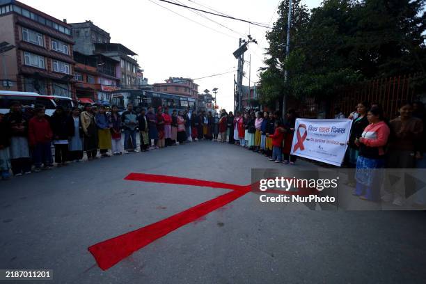 Nepali activists stand in front of the red ribbon shape drawn on the street of Kathmandu, Nepal, on November 30 to raise awareness among people on...
