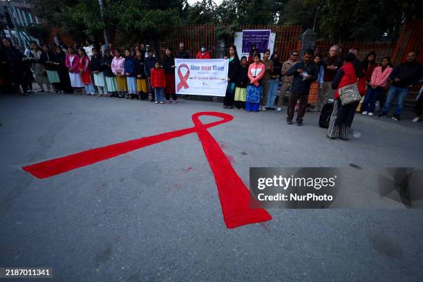 Nepali activists stand in front of the red ribbon shape drawn on the street of Kathmandu, Nepal, on November 30 to raise awareness among people on...