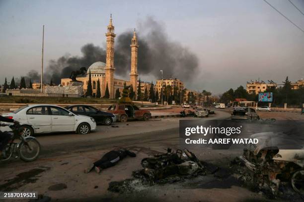 Graphic content / The body of a man is seen next to destroyed cars as smoke billows at the site of Syrian regime airstrikes targeting anti-regime...