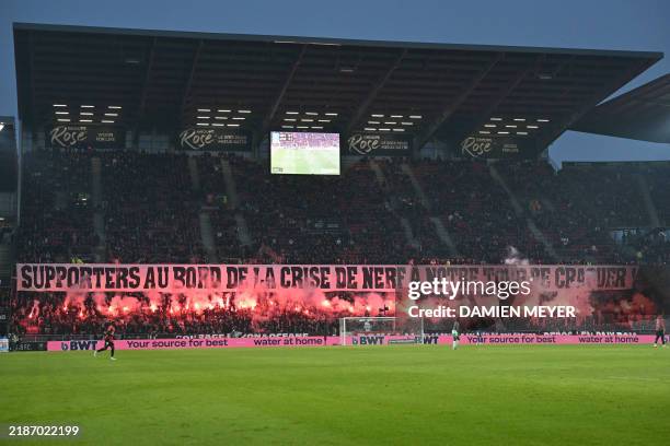 Rennes' players hold a banner reading "Supporters on the verge of a nervous breakdown, it's our turn to crack!" as they light smoke flares during the...