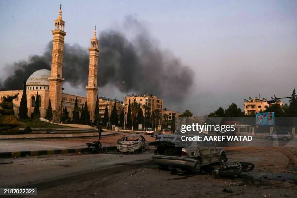 Smoke billows in the distance as damaged cars are seen at the site of Syrian regime airstrikes targeting anti-regime fighters in Aleppo, in northern...