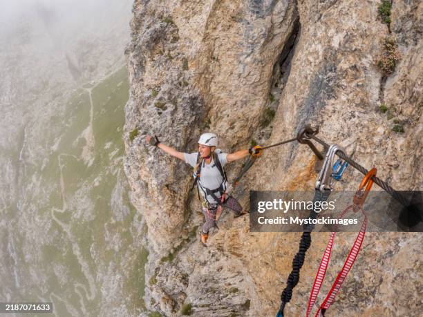 escalador aventurero que navega por un acantilado rocoso con equipo de seguridad en un día de niebla - una mujer de mediana edad solamente fotografías e imágenes de stock